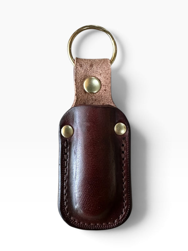 A dark brown leather key fob case with a brass key ring and brass rivets, shown on a clean white background.