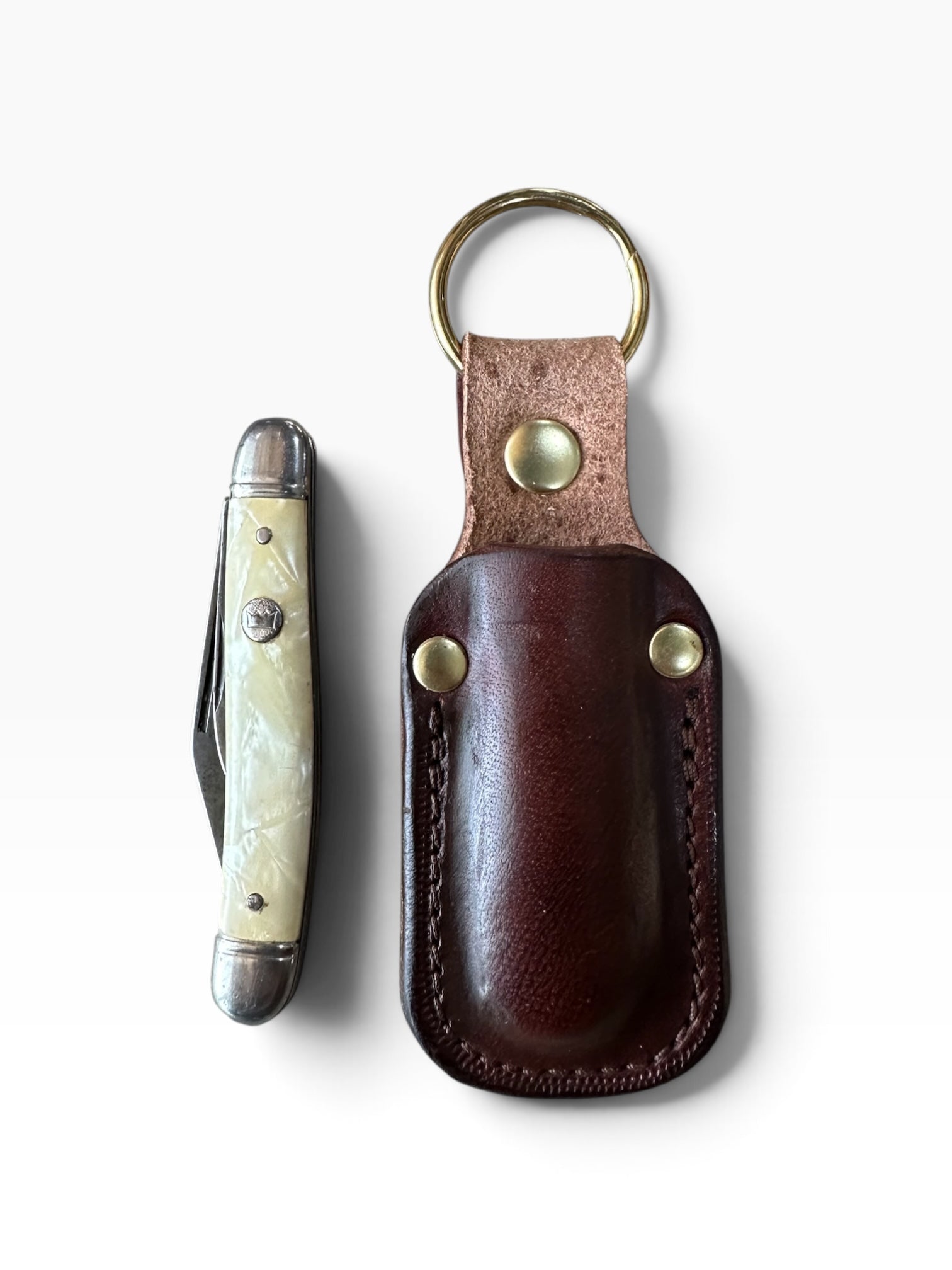 A pocket knife with a cream bone handle and silver-toned metal blade, shown next to its dark brown leather sheath on a white background.