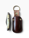 A pocket knife with a cream bone handle and silver-toned metal blade, shown next to its dark brown leather sheath on a white background.